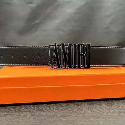 A black leather belt with a large metal logo buckle on an orange background