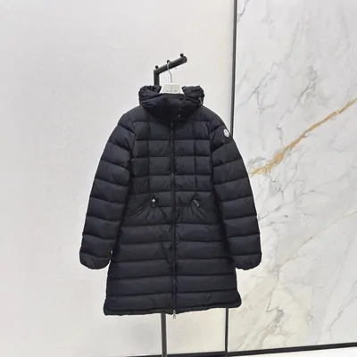 A long black quilted coat on a hanger against a marble wall